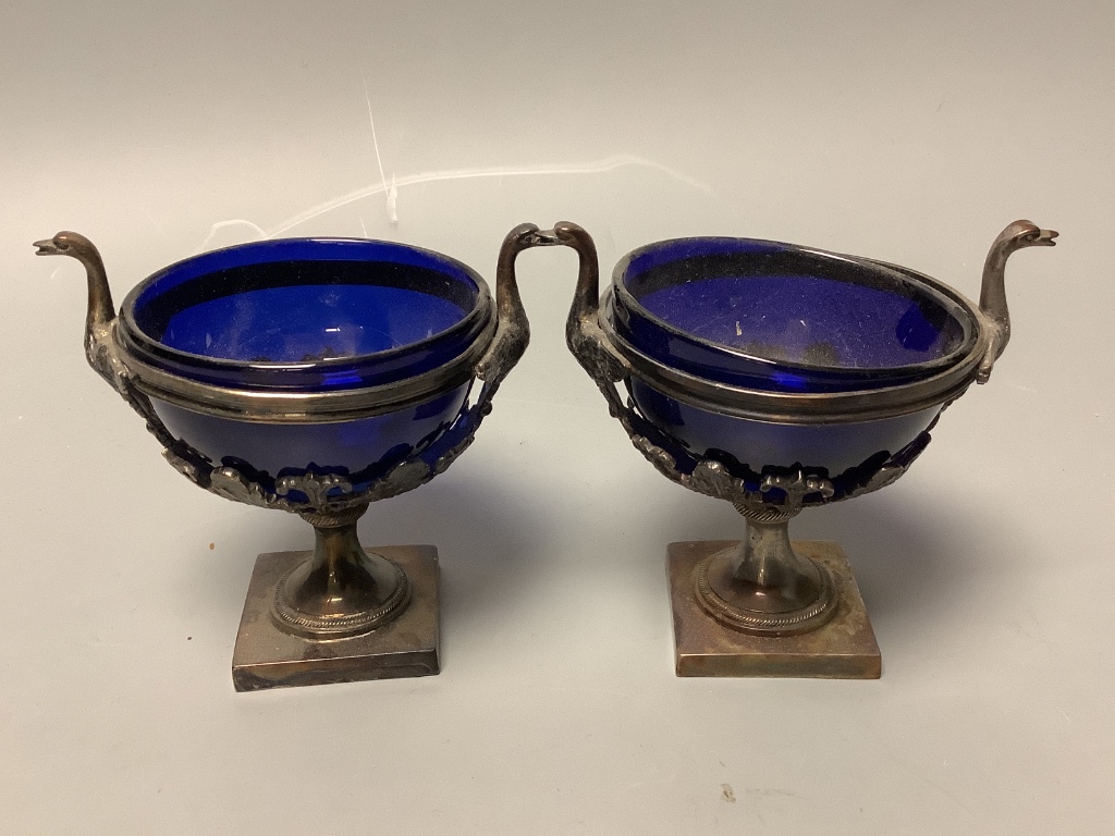 A set of four 19th century French pierced white metal circular pedestal salts with swan neck handles and later? blue glass liners